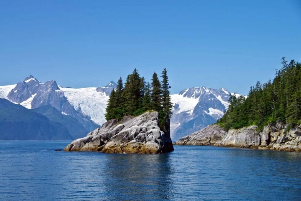 Kenai Fjords sea stack with snow-capped peaks seen from the water