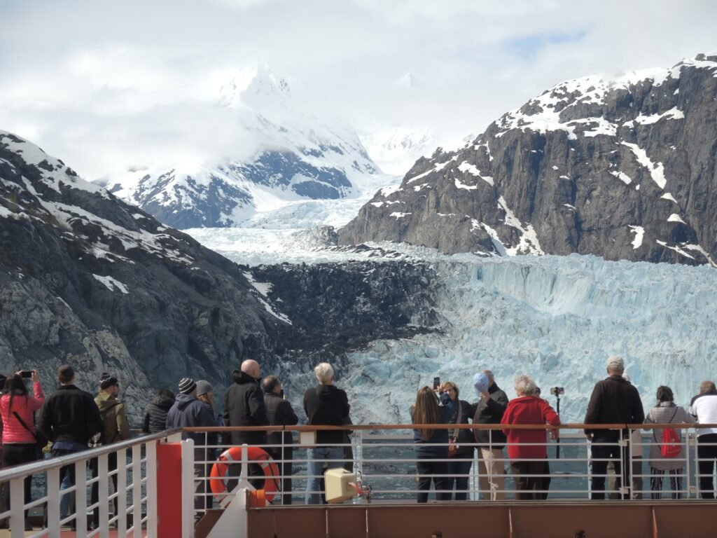 Cruise passengers in jackets at the ship railing watching a tidewater glacier in Alaska.