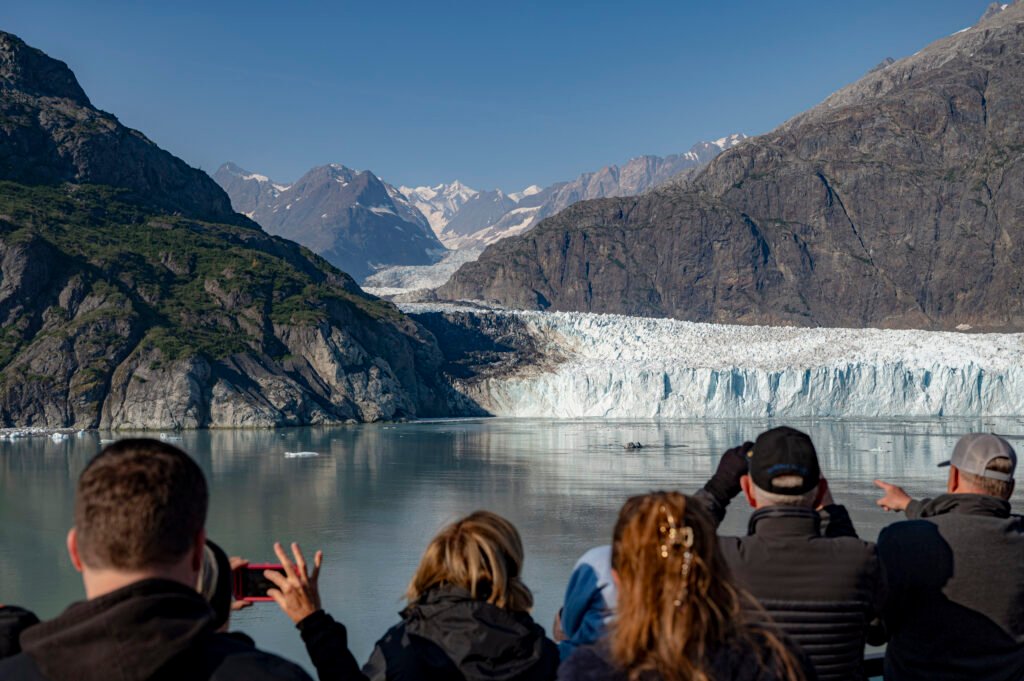 Cruise passengers watching a tidewater glacier flow between steep mountains in Glacier Bay National Park, Alaska.