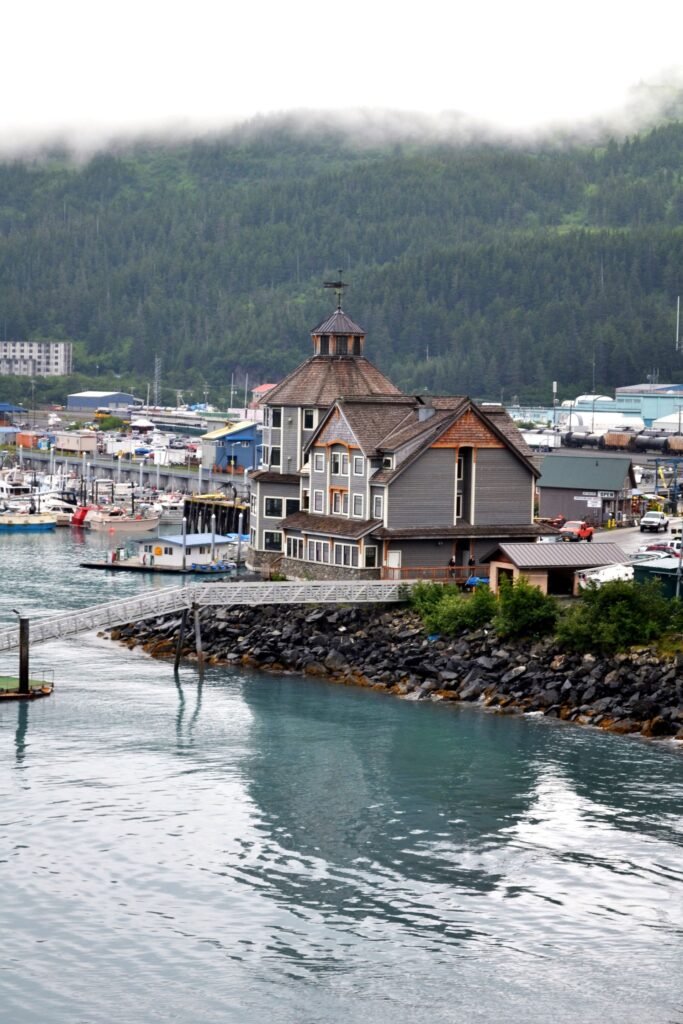 Southeast Alaska harbor town with fishing boats below a forested, cloud-covered hillside